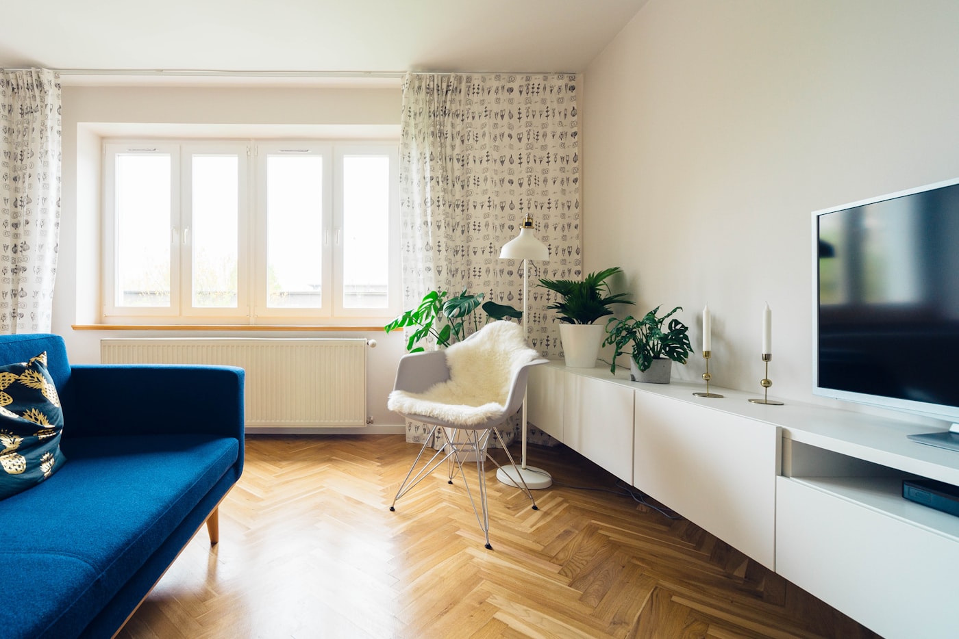 Soggiorno luminoso con parquet a spina, divano blu e affaccio sul verde